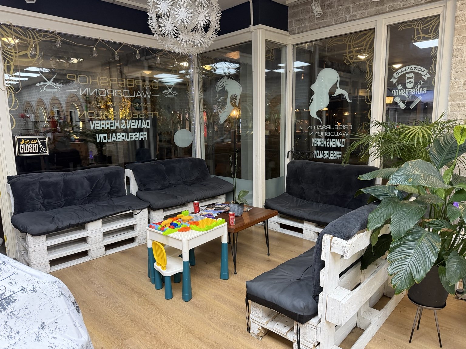 Wartelounge mit hellen Sofas, Holztisch, Zimmerpflanzen und Kinderspielecke